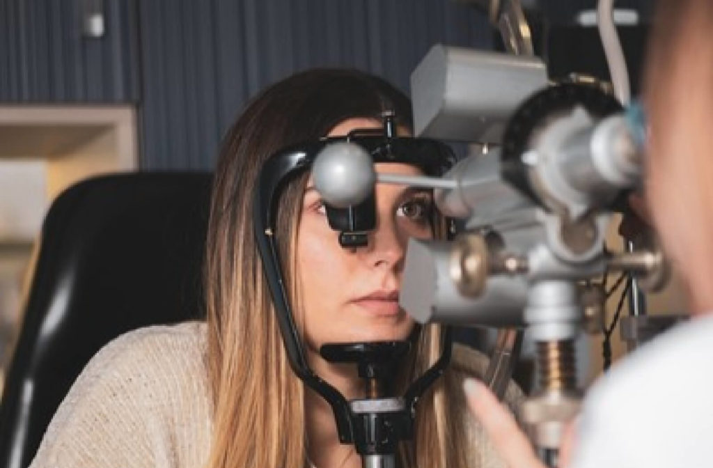 A close-up woman sitting on a chair and looking through a keratometer while an optician measures her corneal radii in a clinic.