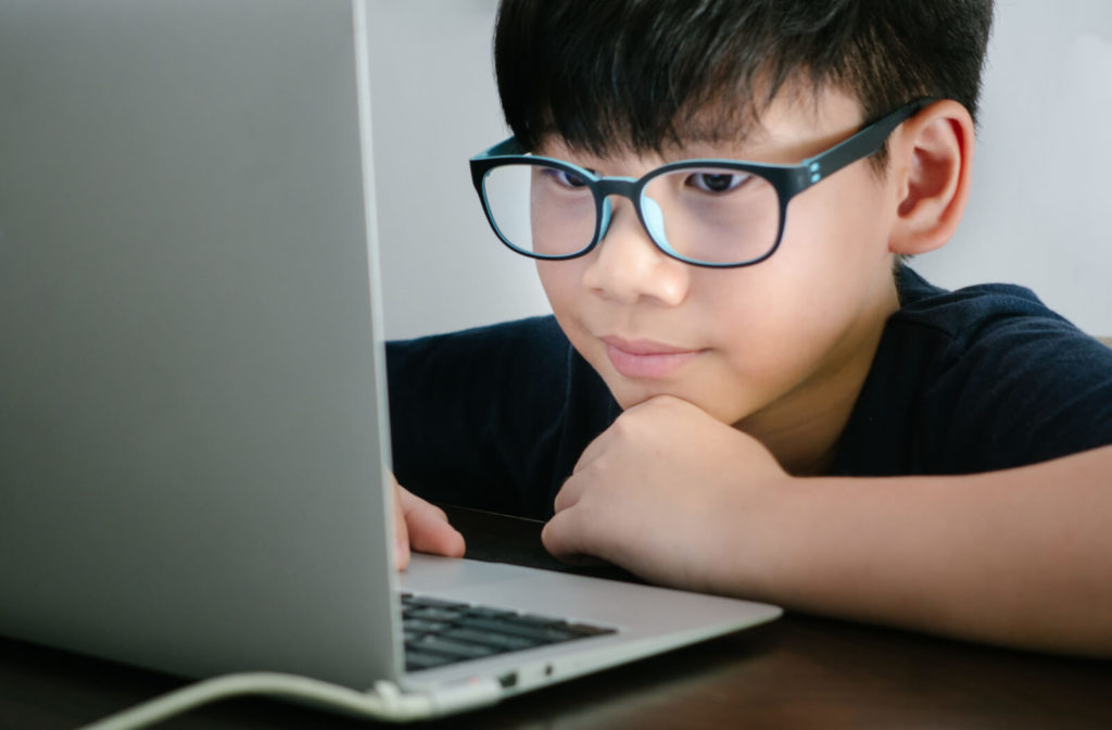 A small boy using blue light glasses while looking at a computer screen.