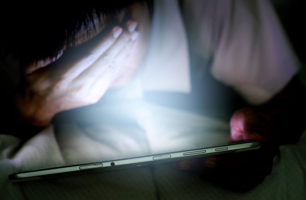 A boy is covering his strained eyes from long exposure to blue light from his tablet pc.
