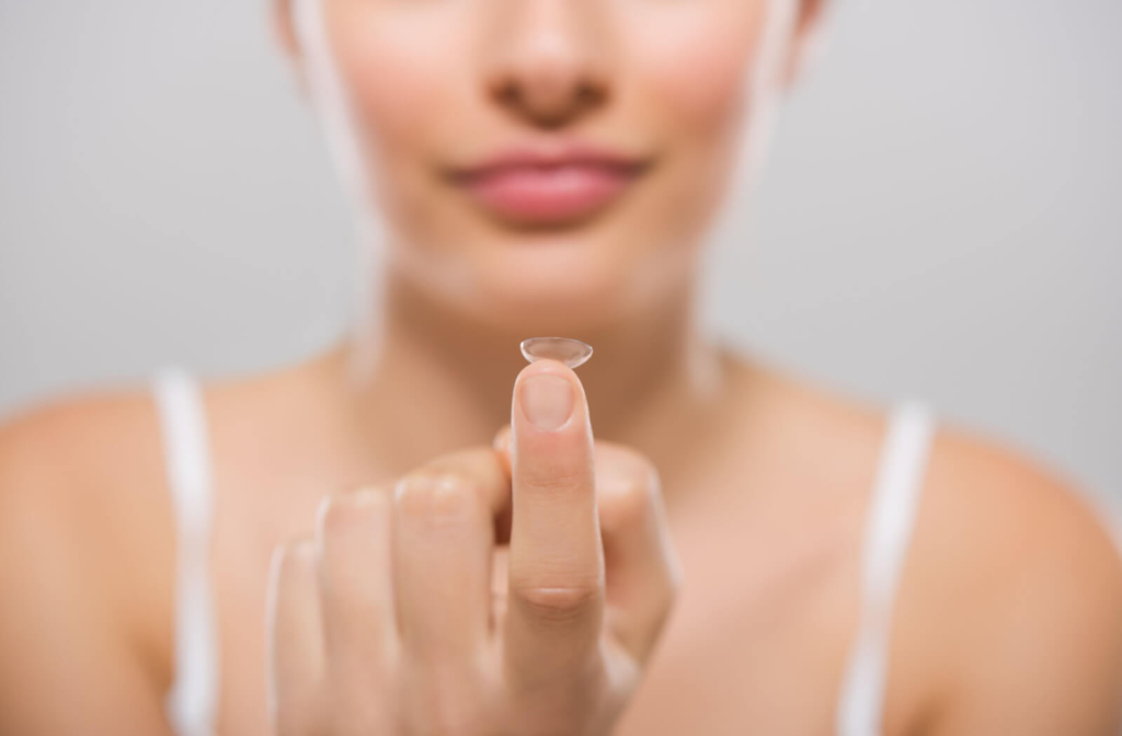 A lady holding up a contact lens on her finger.