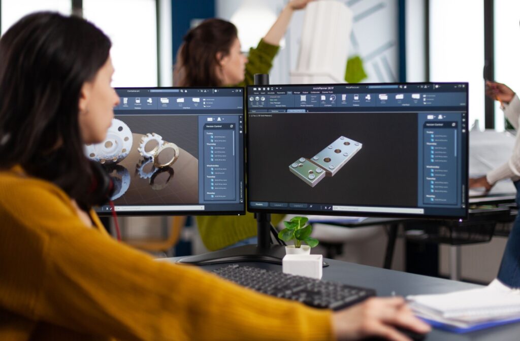 A woman working at her desk while using 2 computer screens.