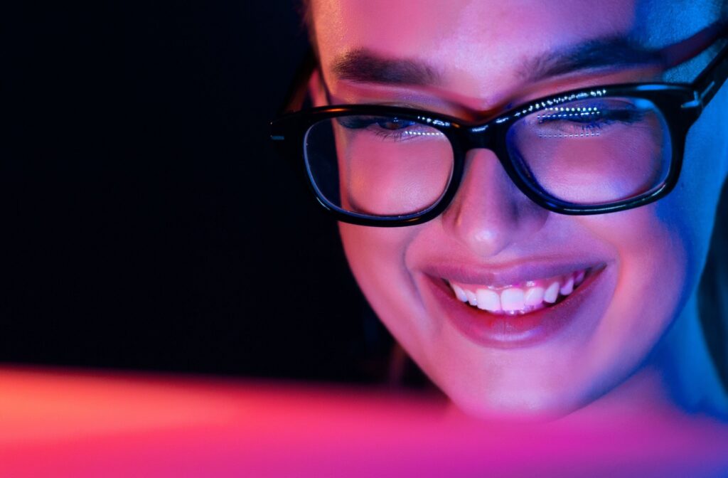 A close-up of a woman with glasses smiling and looking into her computer.