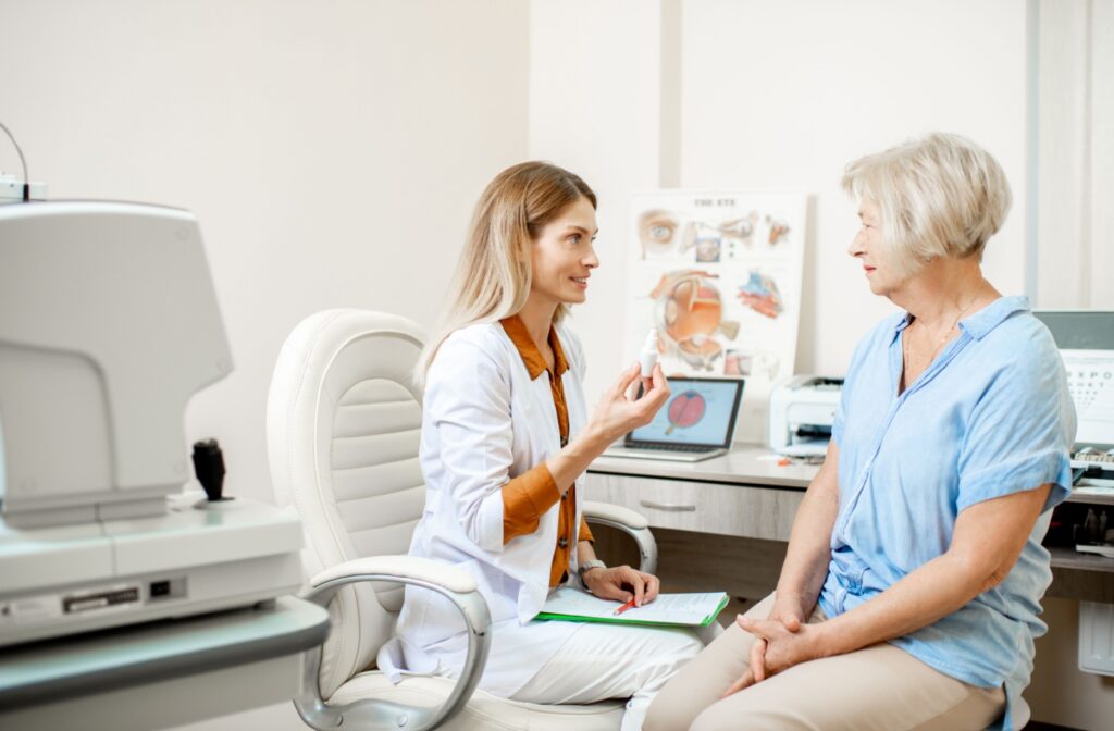 An optometrist talking to a patient after an eye exam while holding up a bottle of eye drops for blepharitis.