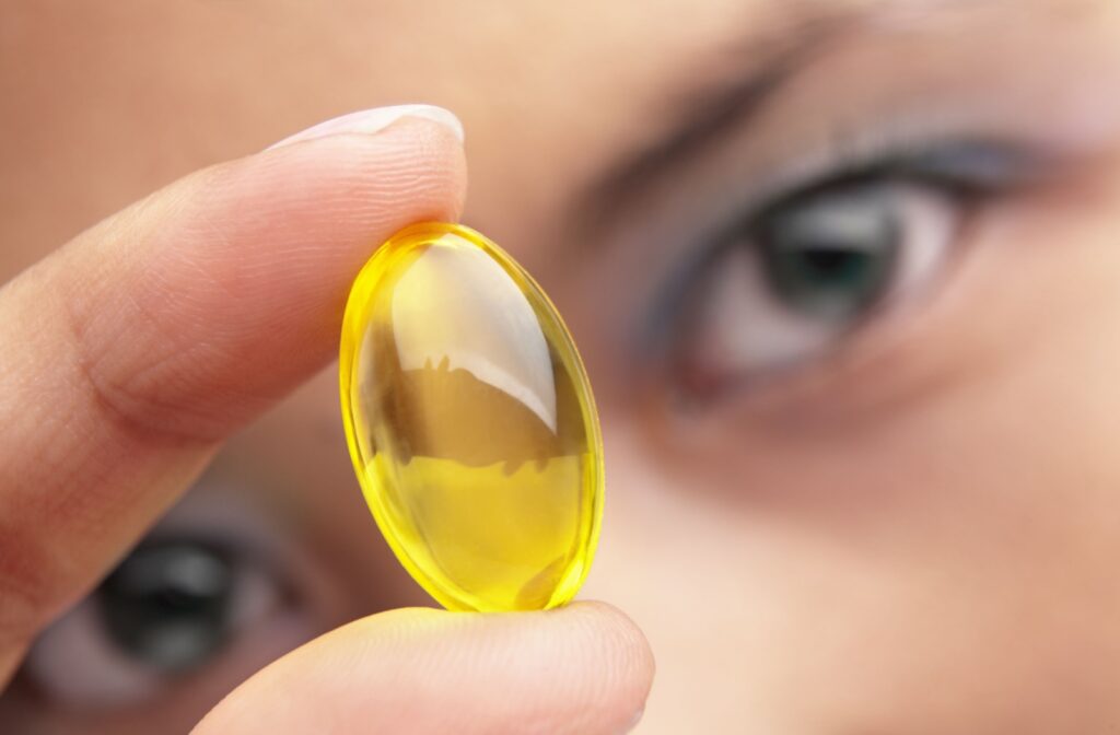 Close-up of yellow supplement pill held by fingers in front of a person's eyes.