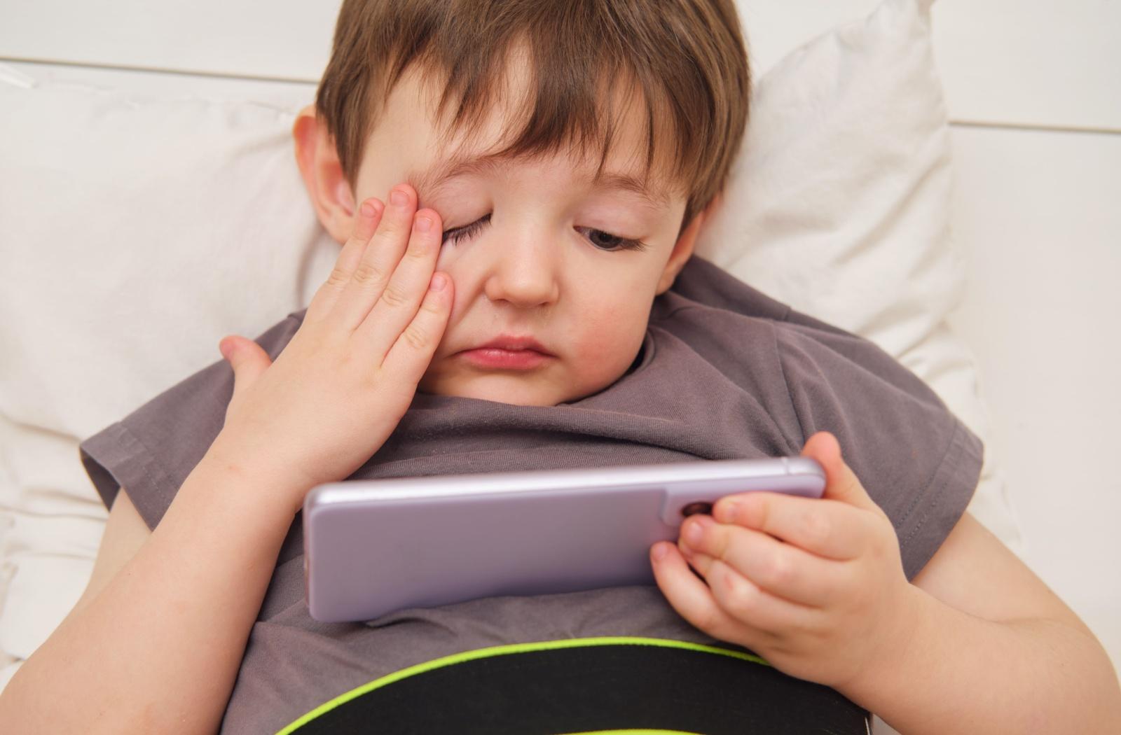 Child rubbing one eye while using a tablet, showing signs of eye strain from screen time.