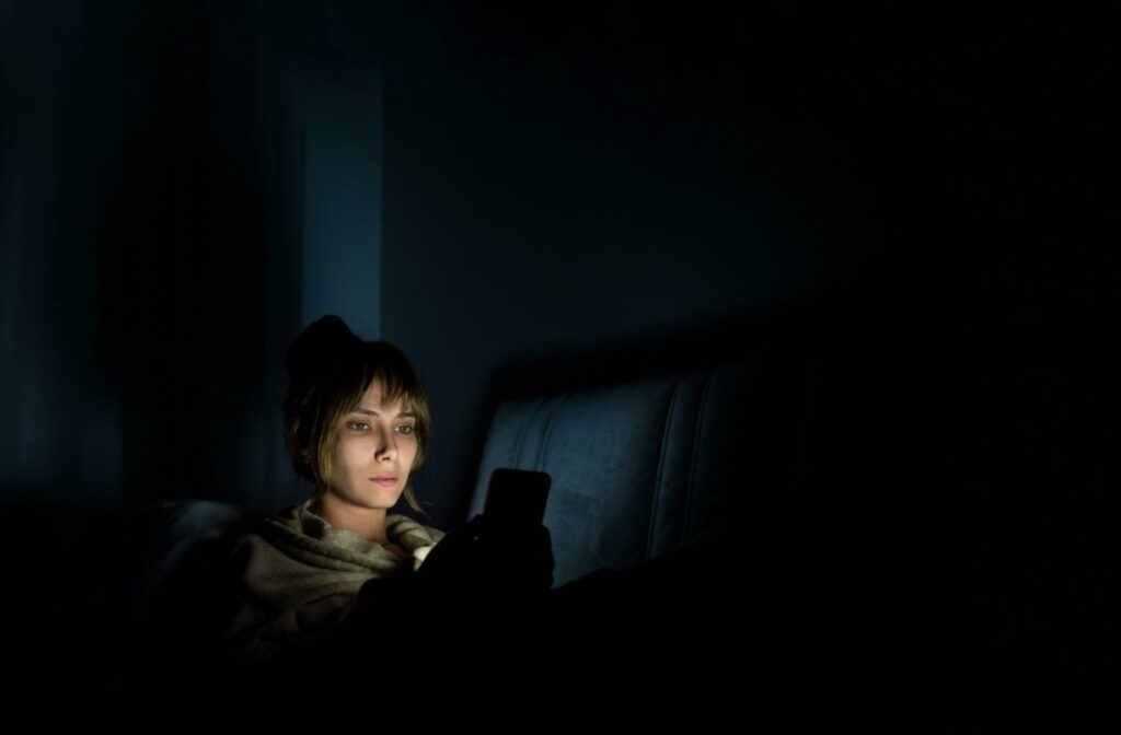Person looking at a phone in bed in a dark room, highlighting how nighttime screen time can affect vision.